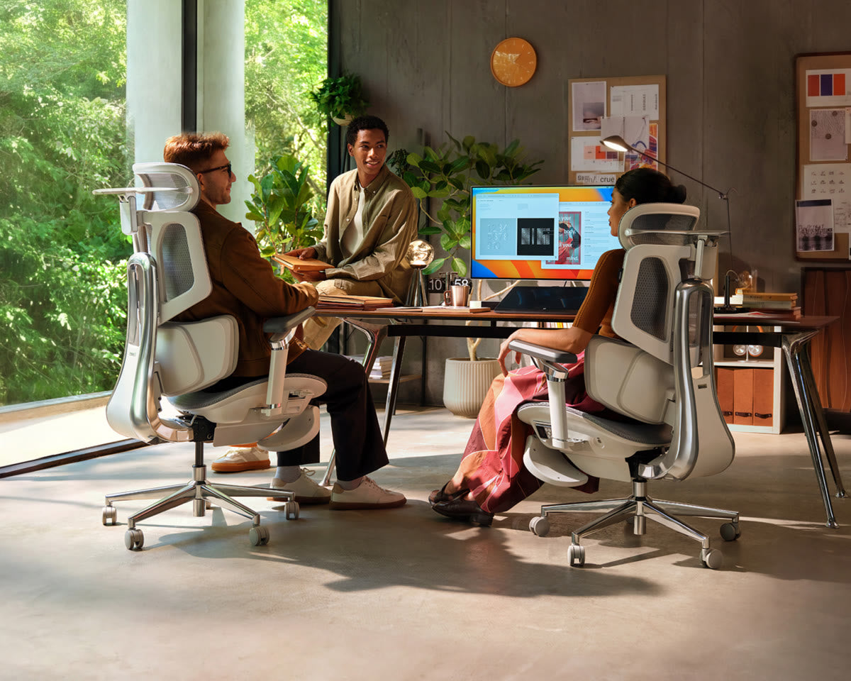 Two people testing ergonomic office chairs in a bright home workspace